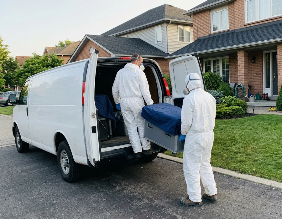 Two technicians in PPE unloading covered equipment from an unmarked van outside a family home