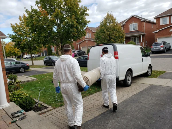Crew carrying sealed rolled carpet to an unmarked van