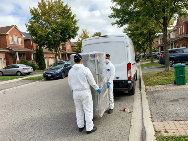 Crew carrying a wrapped old fridge to an unmarked van