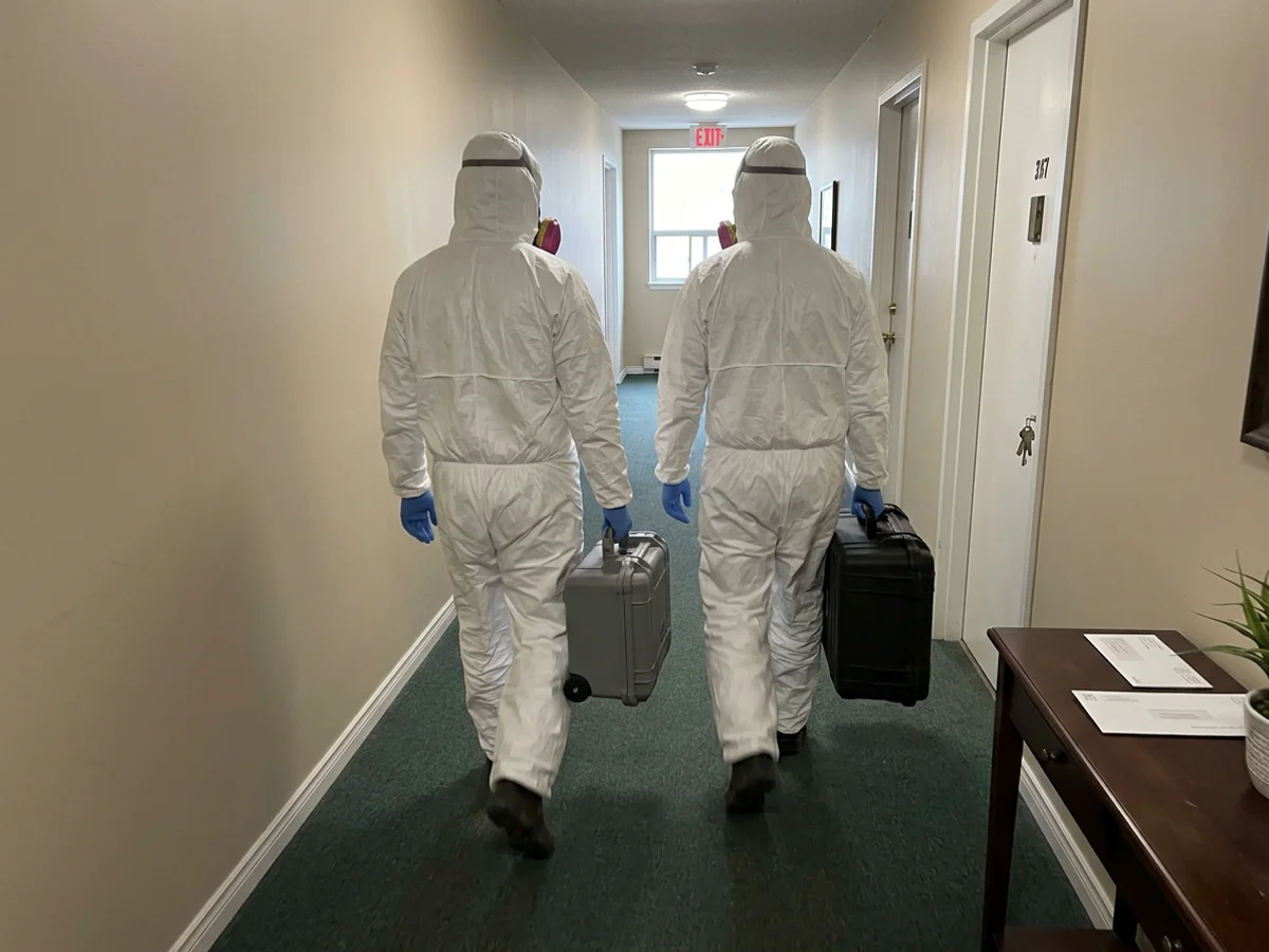 Two remediation technicians in full PPE entering an apartment hallway with covered equipment